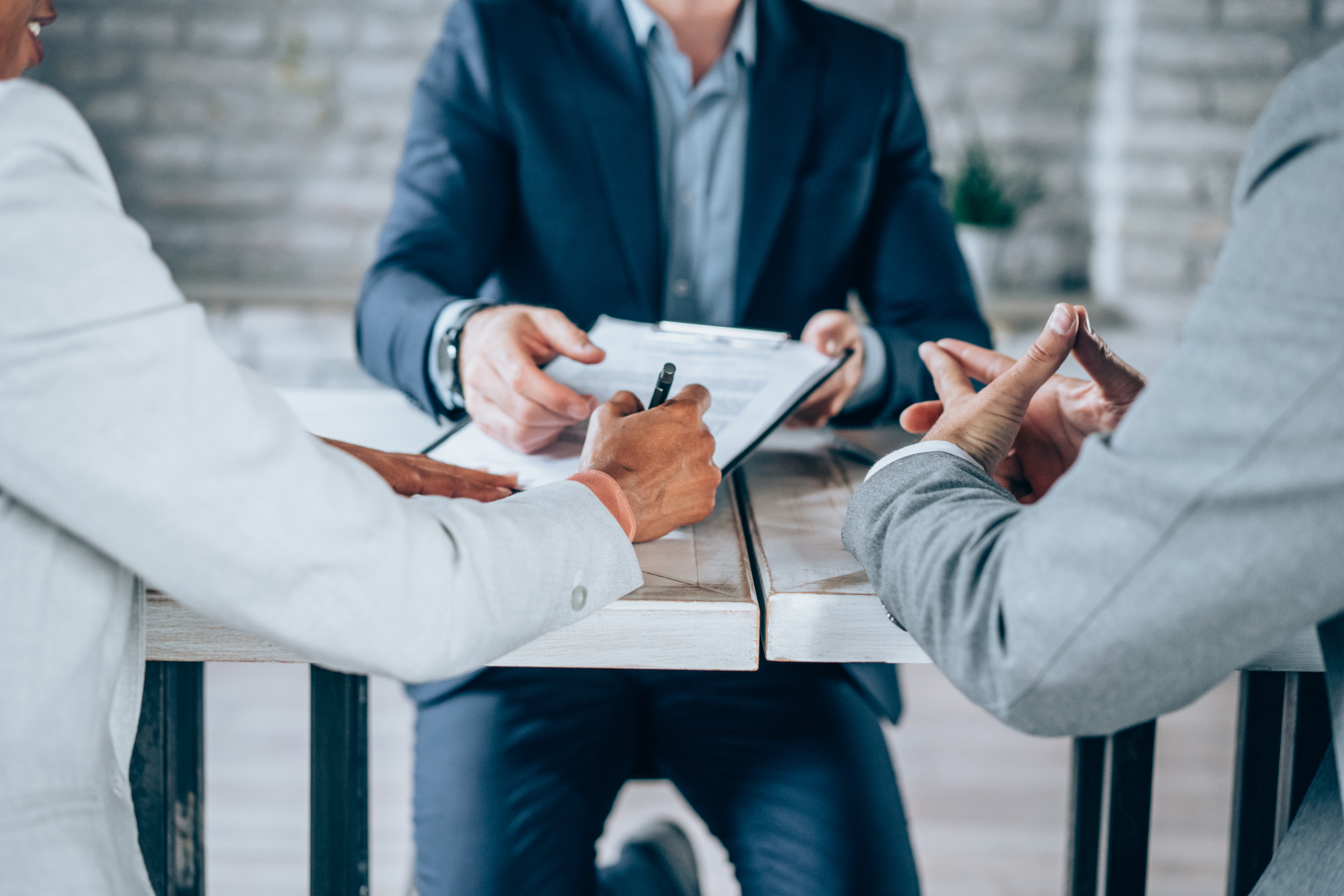 One person sitting across a desk from to other people while handing one person documents to sign
